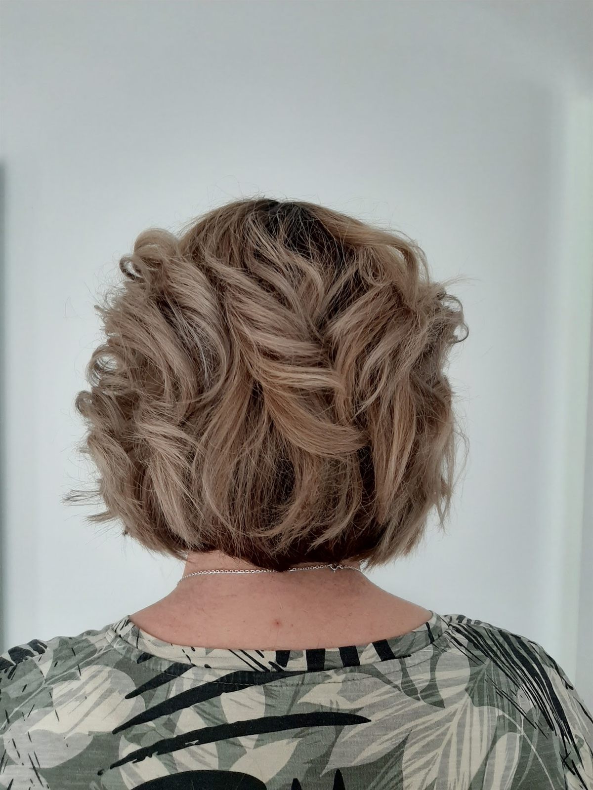 Kort asblond haar met losse krullen, van achteren gezien