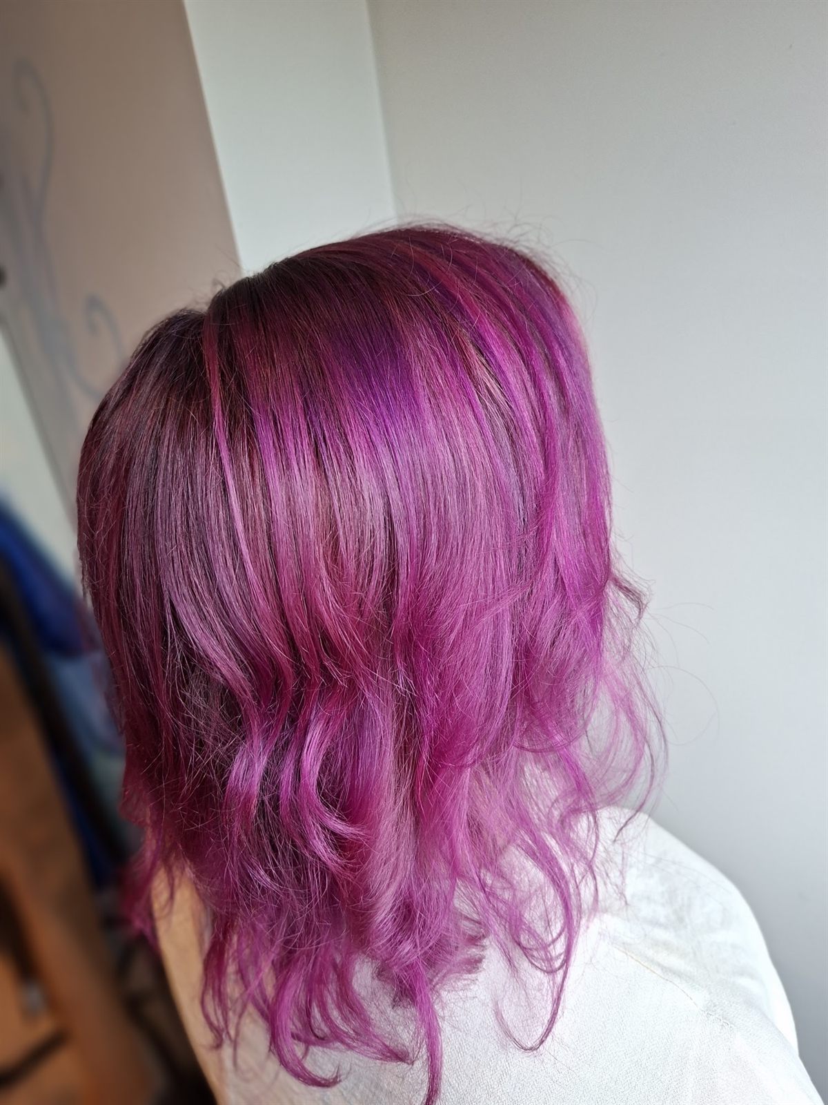 Schouderlang haar in een felle paarsroze kleur met zachte golven