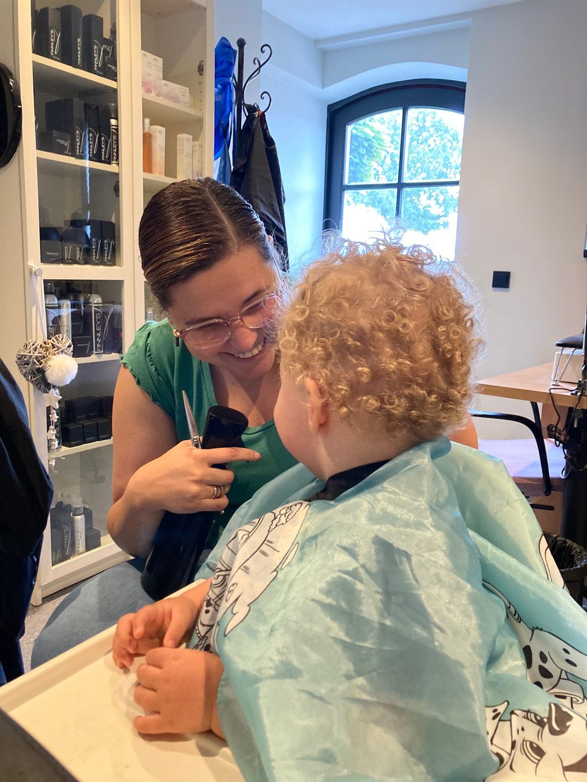 Een kleine klant met krullen krijgt een knipbeurt in de salon